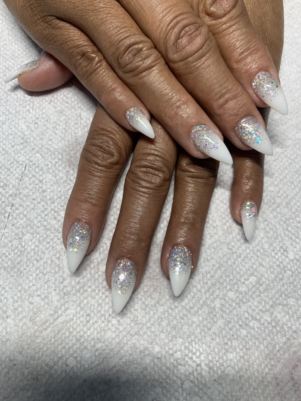 White stiletto nails with silver glitter fading up from the tips